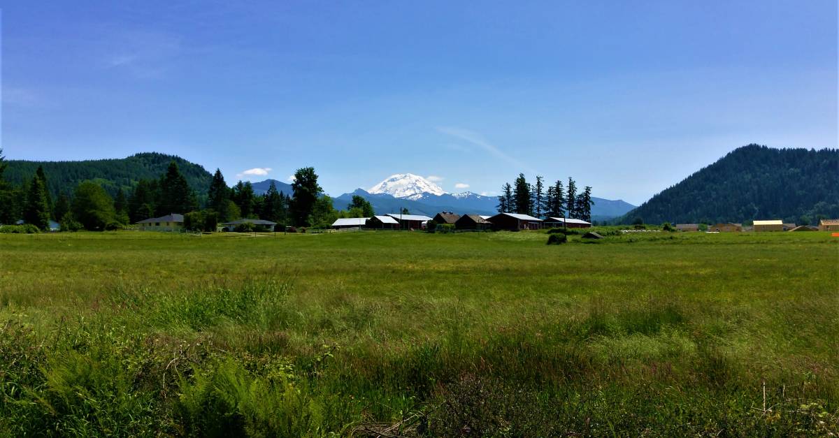 Phot of an open field with a farm and mountain in the distance