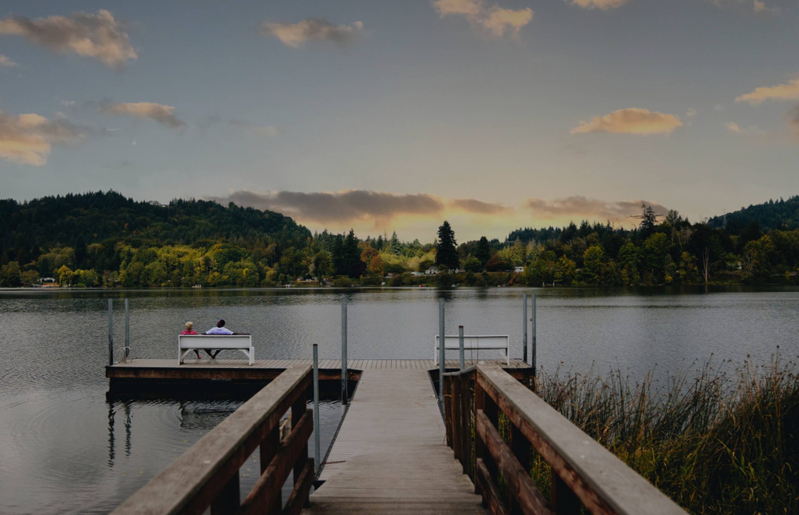 A couple sitting on a dock watching the sunset